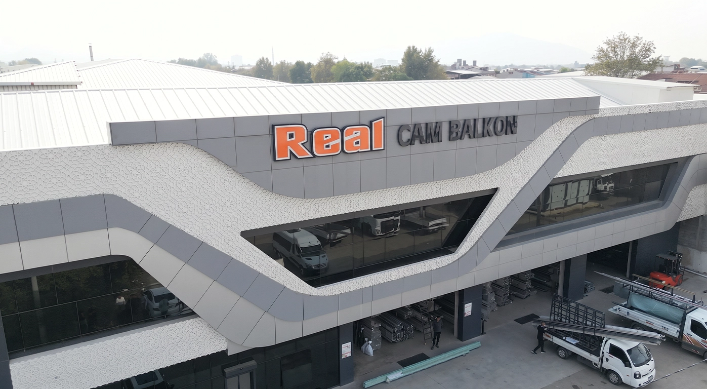 real cam balkon - Bursa Modern commercial building with a bold orange 'Real' sign and a zigzag white facade; loading area and vehicles visible.