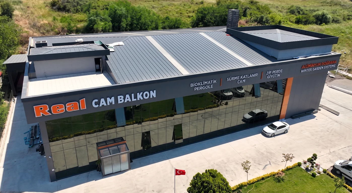 real cam balkon - Yalova Showroom building with large glass facade reading 'Real CAM BALKON', parked cars, Turkish flag, and landscaped front area seen from above