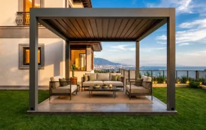 bioklimatik sistem-real cam balkon Outdoor patio under a dark metal pergola with beige cushioned sofas and a coffee table, overlooking the sea and mountains beyond.